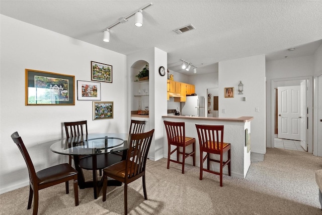 dining space featuring a textured ceiling, light colored carpet, and track lighting