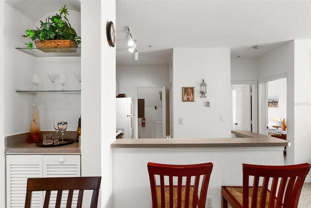 kitchen with white refrigerator, a textured ceiling, and a kitchen breakfast bar