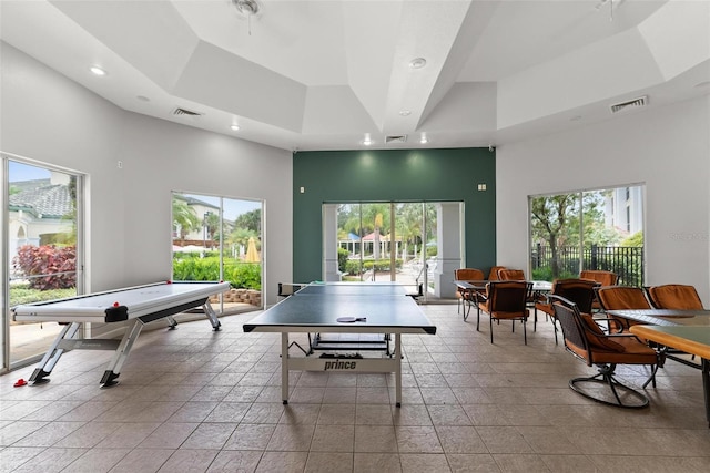 game room with a towering ceiling, a raised ceiling, and a healthy amount of sunlight