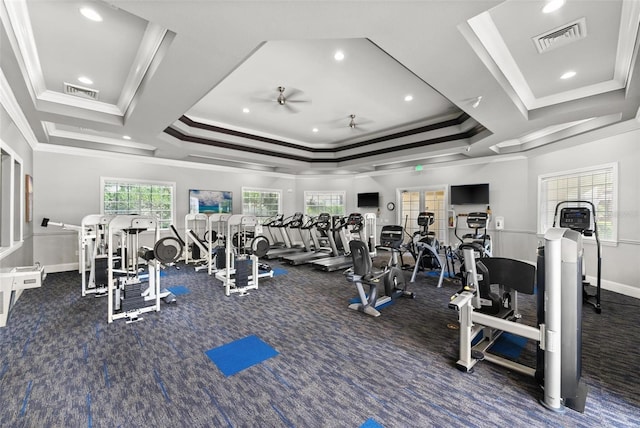 exercise room with ceiling fan, dark colored carpet, a raised ceiling, and ornamental molding