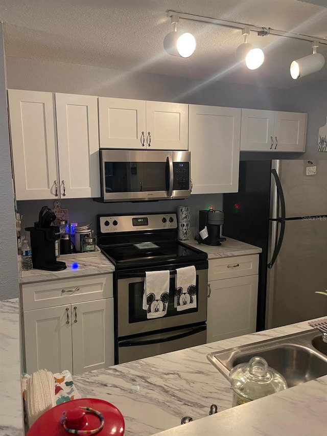 kitchen with appliances with stainless steel finishes, track lighting, and white cabinetry