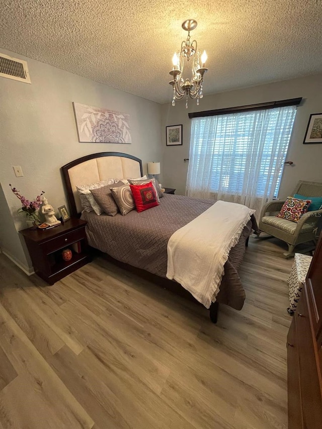 bedroom with an inviting chandelier, a textured ceiling, and wood-type flooring