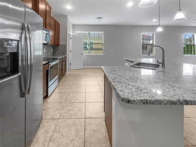 kitchen with decorative light fixtures, stainless steel appliances, a center island with sink, and sink