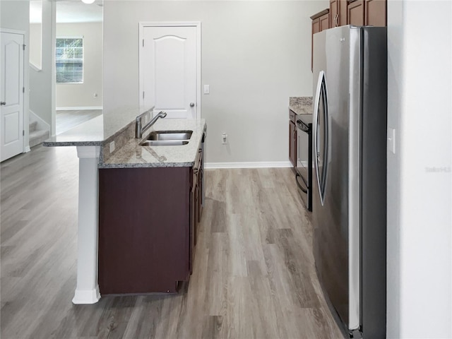 kitchen with light wood-style flooring, a sink, freestanding refrigerator, and baseboards