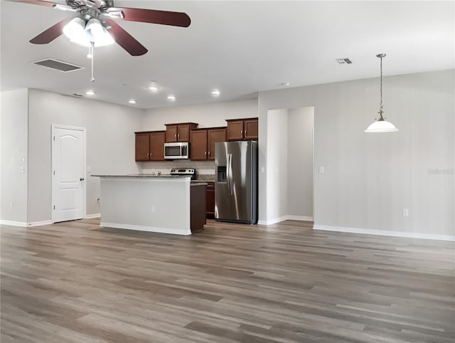 kitchen with visible vents, a kitchen island, open floor plan, decorative light fixtures, and stainless steel appliances