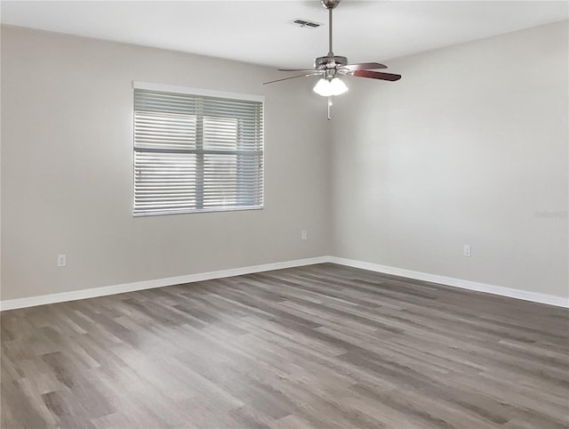 empty room featuring visible vents, dark wood finished floors, baseboards, and ceiling fan