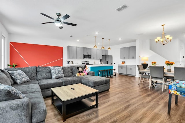 living room featuring ceiling fan with notable chandelier and hardwood / wood-style floors