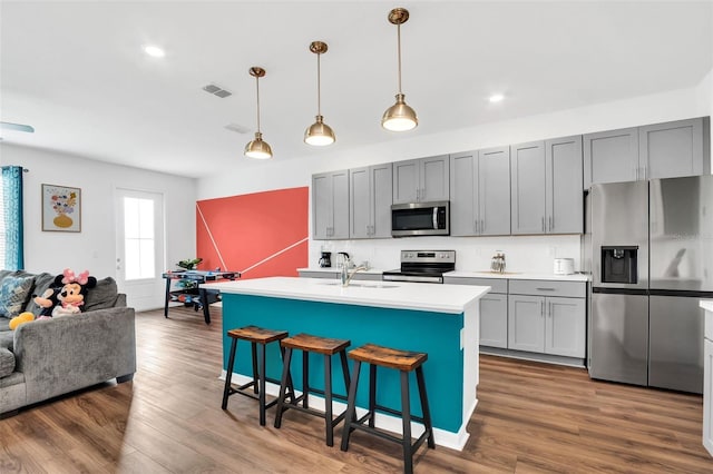 kitchen with a kitchen bar, appliances with stainless steel finishes, hanging light fixtures, an island with sink, and hardwood / wood-style flooring