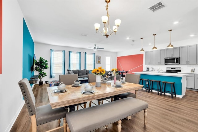 dining room with ceiling fan with notable chandelier and light hardwood / wood-style flooring