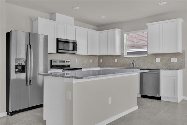 kitchen with appliances with stainless steel finishes, white cabinetry, light tile patterned floors, and a kitchen island