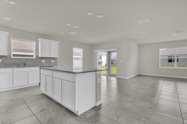 kitchen with light tile patterned flooring, a kitchen island, white cabinets, and dark stone countertops