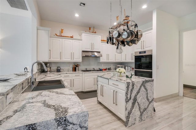 kitchen with white cabinetry, light hardwood / wood-style flooring, a center island, black double oven, and sink