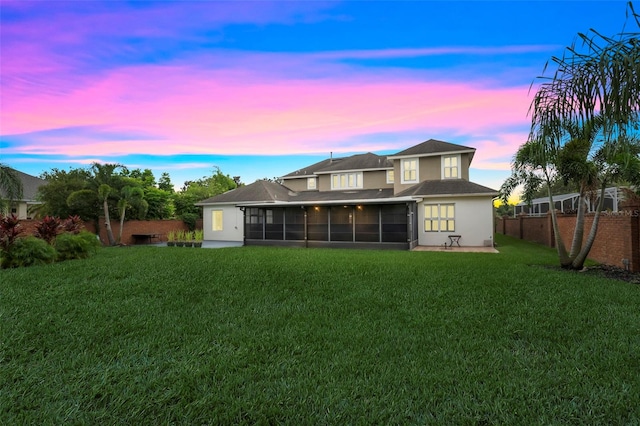 back house at dusk featuring a sunroom and a lawn