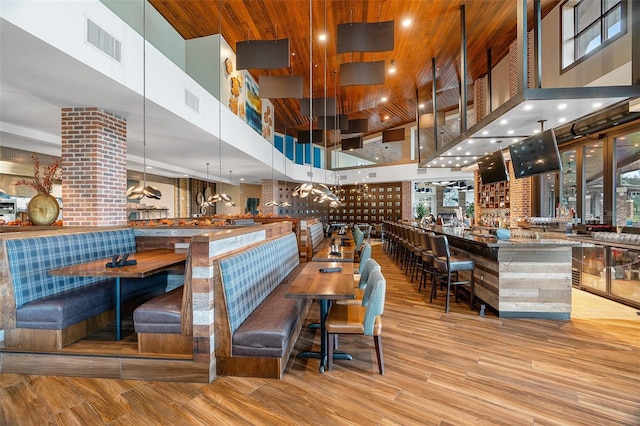 bar featuring a high ceiling, hanging light fixtures, wooden ceiling, and light hardwood / wood-style floors