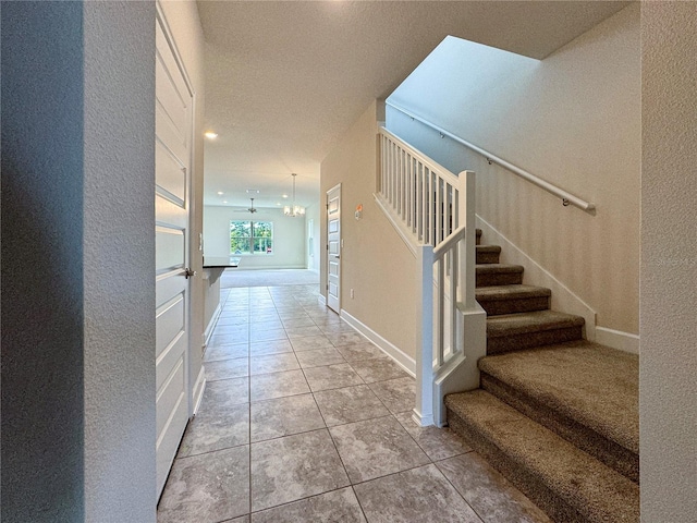 hall with an inviting chandelier, a textured ceiling, and light tile patterned floors