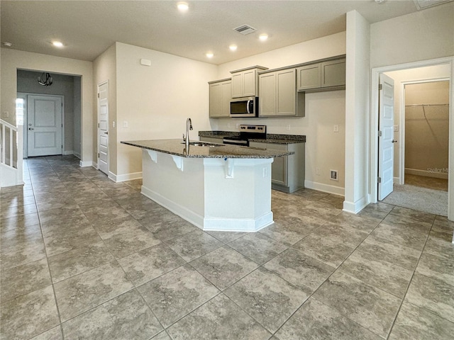 kitchen with gray cabinets, an island with sink, sink, dark stone countertops, and stainless steel appliances