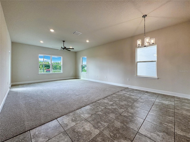 spare room with ceiling fan with notable chandelier, dark carpet, and a textured ceiling