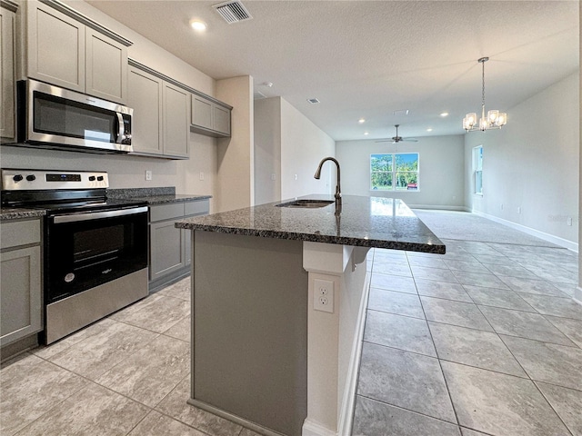 kitchen with sink, appliances with stainless steel finishes, gray cabinets, dark stone counters, and a kitchen island with sink