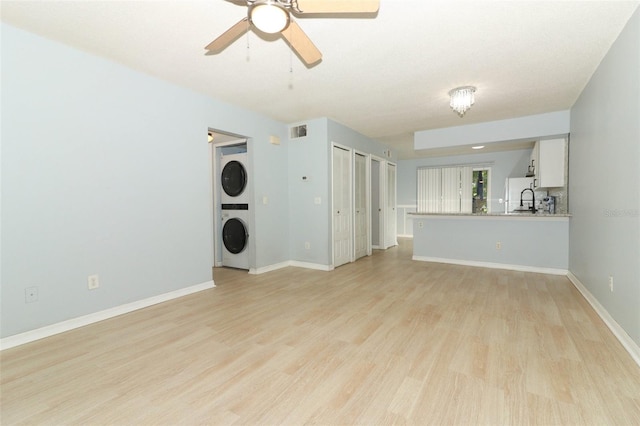 unfurnished living room with stacked washer and dryer, light wood-style flooring, visible vents, and baseboards