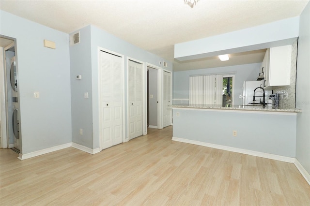 interior space with light wood-style flooring, white cabinetry, baseboards, freestanding refrigerator, and stacked washer and clothes dryer