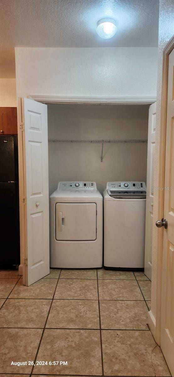 laundry area featuring washing machine and clothes dryer, light tile patterned floors, and a textured ceiling