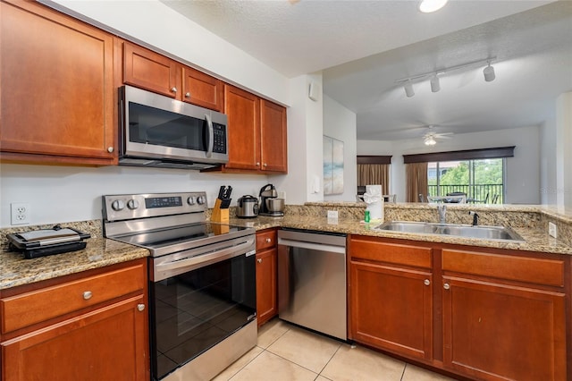 kitchen featuring light stone counters, track lighting, appliances with stainless steel finishes, light tile patterned flooring, and sink