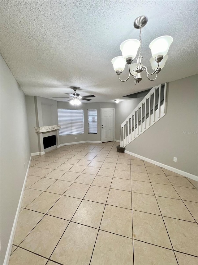 unfurnished living room featuring a textured ceiling, light tile patterned flooring, and ceiling fan with notable chandelier