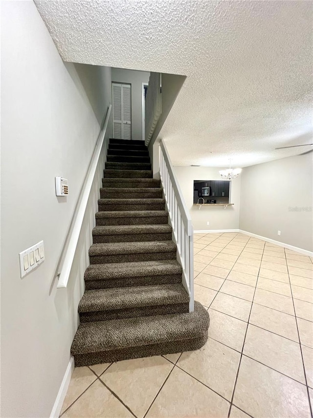 staircase featuring tile patterned flooring, a textured ceiling, and a chandelier