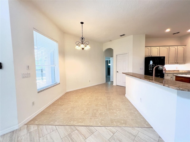 kitchen with sink, black fridge, dark stone countertops, pendant lighting, and a notable chandelier