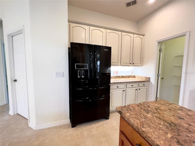 kitchen featuring black refrigerator with ice dispenser, light tile patterned floors, and light stone counters