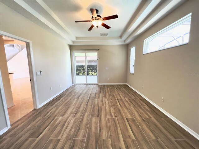 empty room featuring ceiling fan, a tray ceiling, and dark hardwood / wood-style flooring