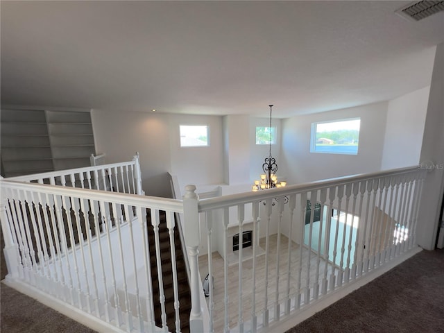 hall with an inviting chandelier, plenty of natural light, and carpet flooring