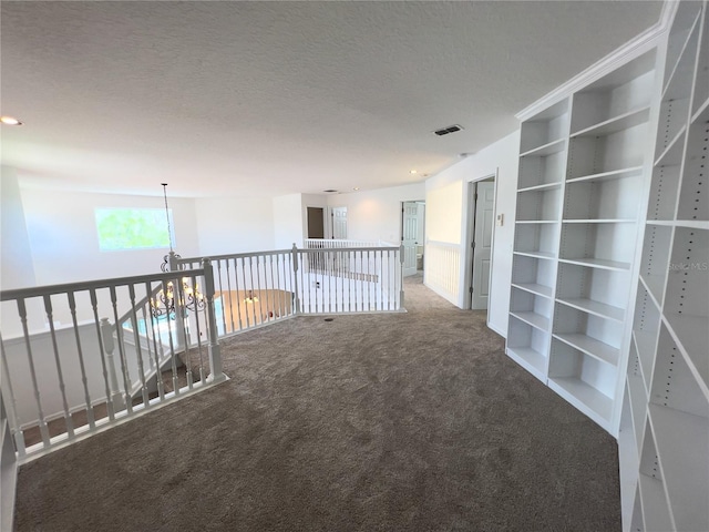 hallway featuring carpet floors, an inviting chandelier, a textured ceiling, and built in features