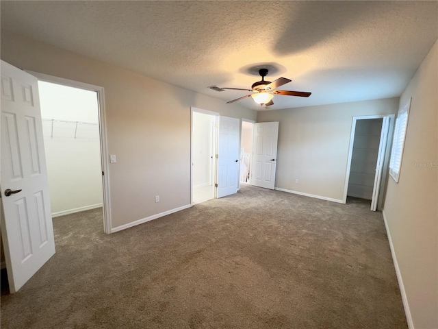 unfurnished bedroom featuring a textured ceiling, a spacious closet, ceiling fan, a closet, and dark colored carpet