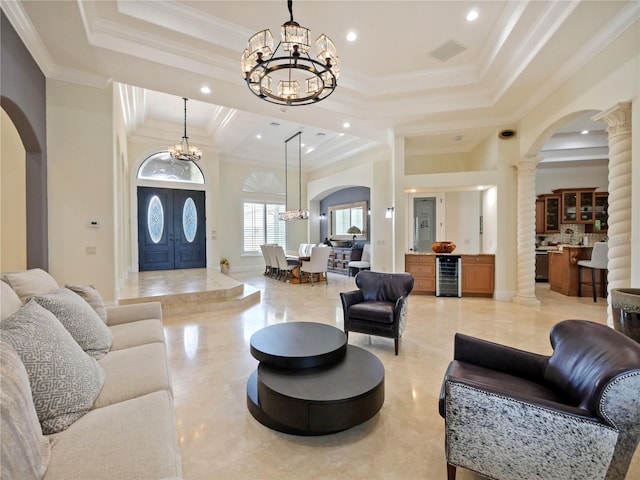 living room featuring a towering ceiling, decorative columns, beverage cooler, crown molding, and an inviting chandelier