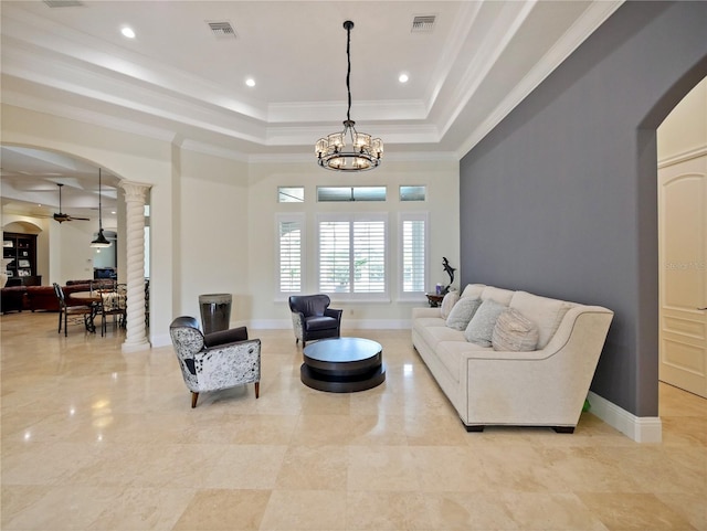 living room with decorative columns, crown molding, a tray ceiling, and ceiling fan with notable chandelier