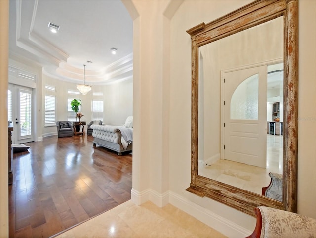 foyer with a raised ceiling, wood-type flooring, a notable chandelier, and ornamental molding