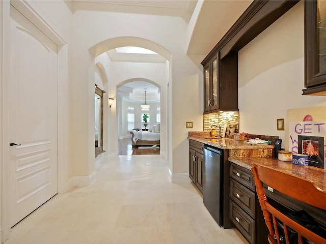 bar featuring backsplash, light stone counters, dark brown cabinets, and dishwasher