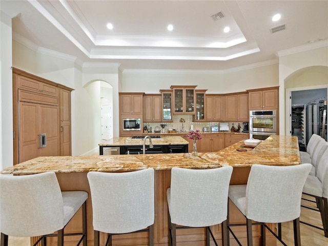 kitchen with a breakfast bar area, a large island with sink, light stone counters, and stainless steel appliances