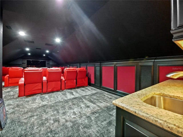 carpeted home theater room with sink and vaulted ceiling