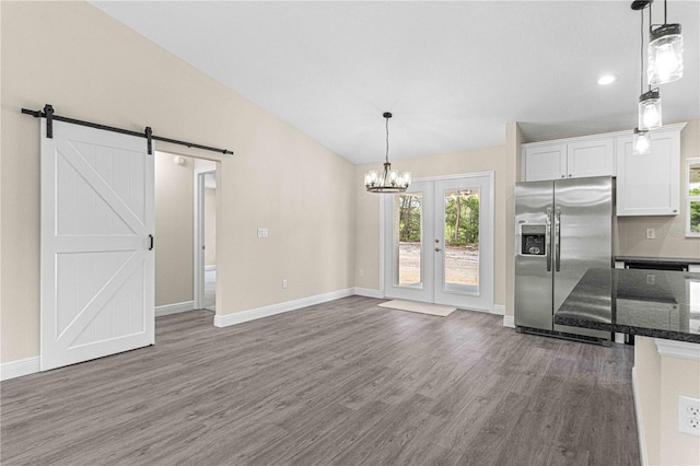 kitchen featuring stainless steel refrigerator with ice dispenser, decorative light fixtures, white cabinetry, vaulted ceiling, and a barn door