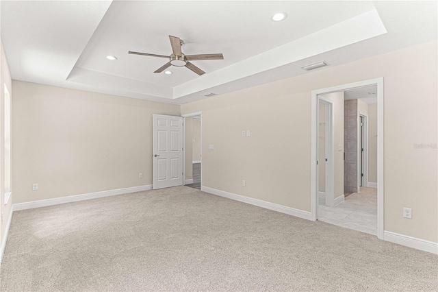 empty room with ceiling fan, light colored carpet, and a tray ceiling