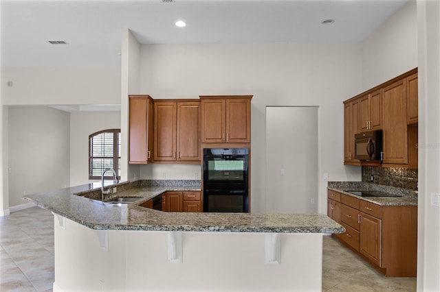 kitchen featuring stone counters, kitchen peninsula, sink, a breakfast bar area, and black appliances