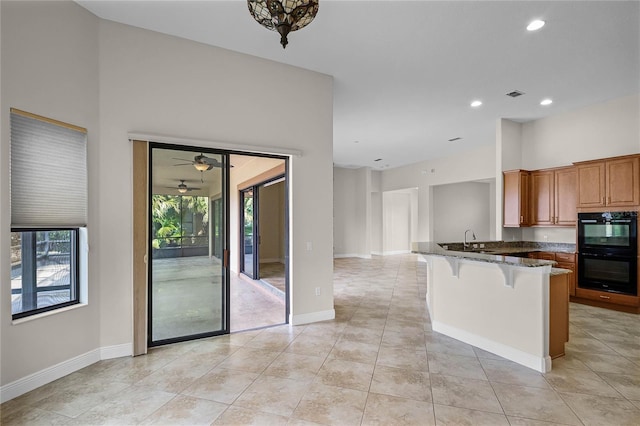 kitchen with a breakfast bar, light tile patterned floors, kitchen peninsula, black double oven, and dark stone counters