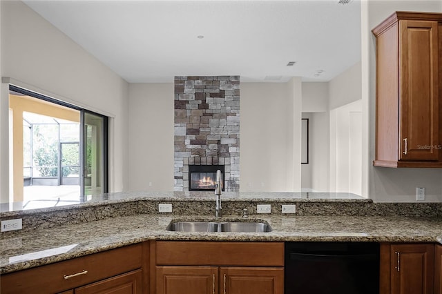 kitchen featuring light stone counters, sink, a fireplace, and black dishwasher