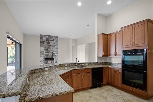 kitchen featuring stone counters, a stone fireplace, sink, light tile patterned floors, and black appliances