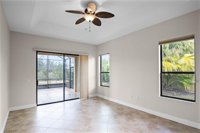 tiled empty room featuring ceiling fan and a tray ceiling