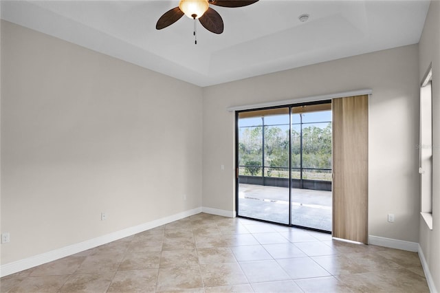 tiled empty room featuring ceiling fan and a tray ceiling