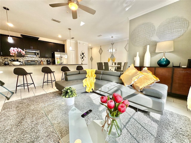 living room with light tile patterned flooring, ceiling fan with notable chandelier, and ornamental molding