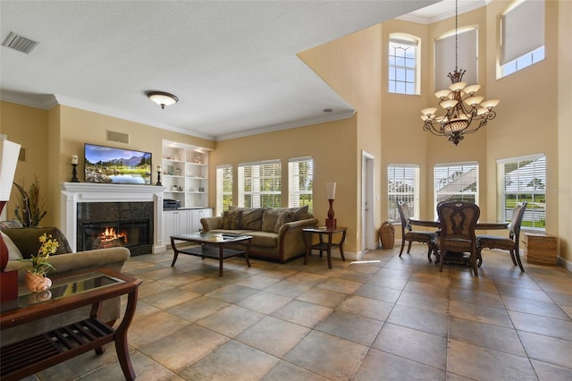 living room featuring built in shelves, a textured ceiling, ornamental molding, a notable chandelier, and a high end fireplace